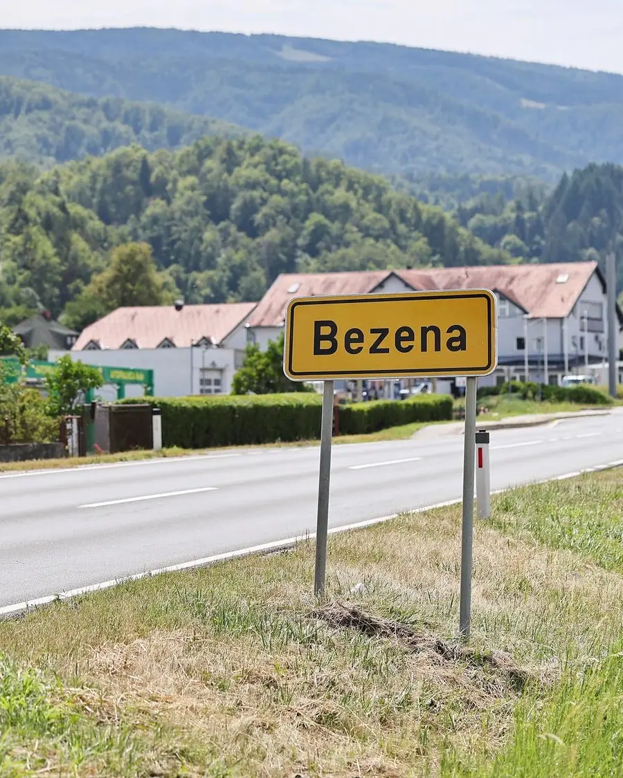 Tabla Bezena ob cesti z naseljem in Pohorjem v ozadju.